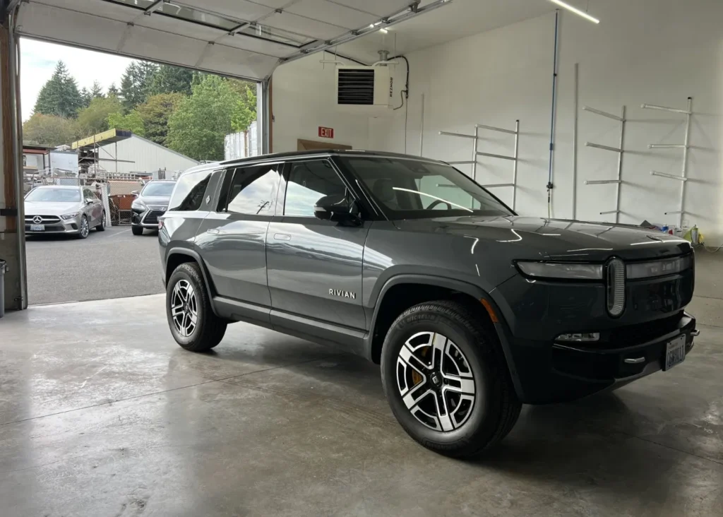Dark gray Rivian R1S electric SUV inside an auto body shop bay for specialized collision repair.