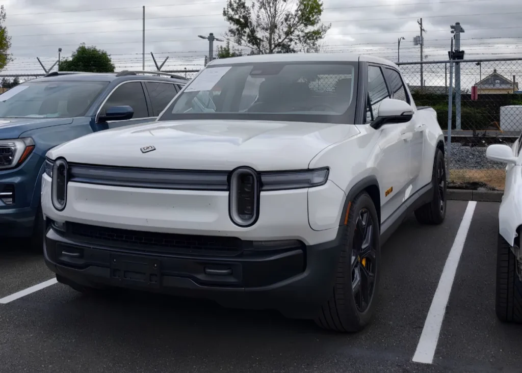 White Rivian R1T electric pickup truck parked in an auto body repair lot.